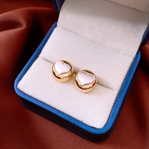 Detailed close-up of golden round heart stud earrings resting in a luxury velvet box