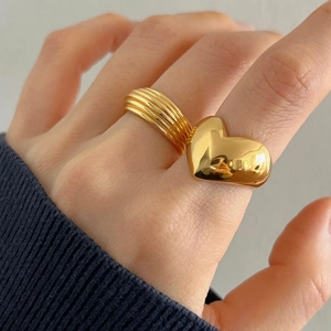 Detail of chunky gold heart ring and textured multi-layer band on female hand
