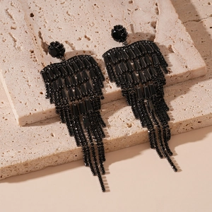 Gros plan de boucles d'oreilles à longs pompons noirs en zircon sur pierre beige texturée