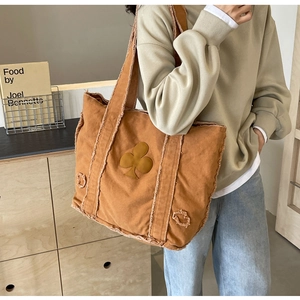Brown canvas tote bag with clover patch and frayed edges worn by model in a casual setting