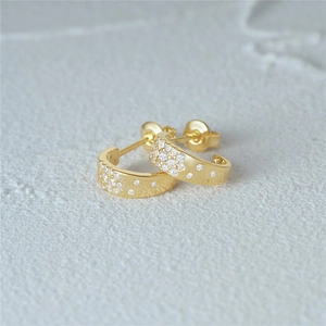 Macro detail of gold C-shape star earrings with sparkling stones on a stone background