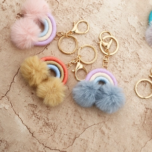 Detail of colorful woven rainbow keychains with soft faux fur pom-poms and golden clips