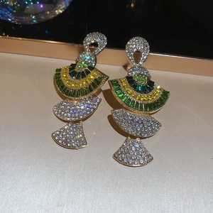 Detailed close-up of fan-shaped golden earrings with green and yellow gemstones