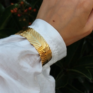Bracciale rigido dorato con trama a piuma esagerata per donna in un ambiente naturale