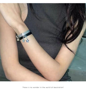 Détail d'un bracelet Y2K à chaîne en maille argentée, cordon noir et pendentifs étoiles