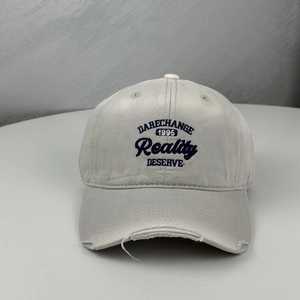 Close-up of embroidered letters on grey distressed cotton baseball cap with ripped brim