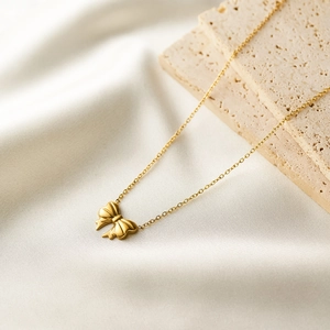Close-up of elegant 18K gold bow necklace on white silk and textured stone background