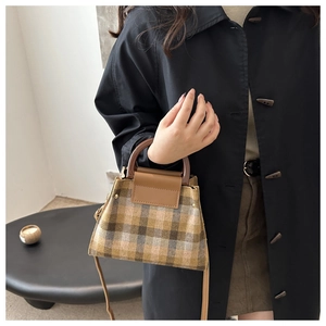 Détail du sac à carreaux vintage avec poignée en résine sur fond de manteau noir