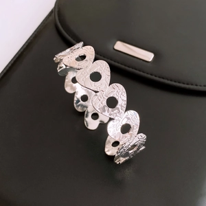 Detail of silver open cuff bracelet featuring hollow heart charms and embossed flowers