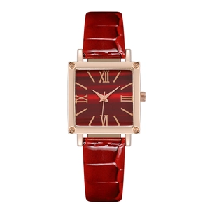 Detail of rose gold square watch face with roman numerals and red leather strap