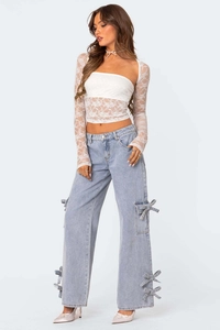 Detail view of light blue wide-leg jeans with decorative bow ties and lace texture top