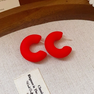 Détail de boucles d'oreilles créoles C rouge mat sur fond de tissu texturé vintage