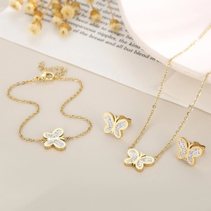 Flat lay of gold butterfly jewelry set including necklace and earrings on beige surface