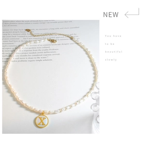 Detail of freshwater pearl necklace with gold letter X pendant on white shell base