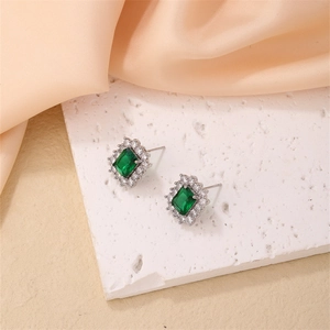 Detailed view of emerald-cut green zircon stud earrings on a textured stone surface