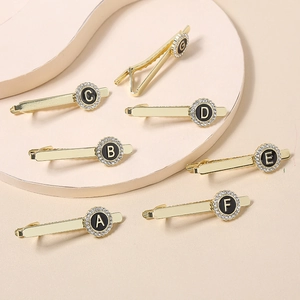 Detail of golden round initial tie clips with rhinestone accents and letters A to G