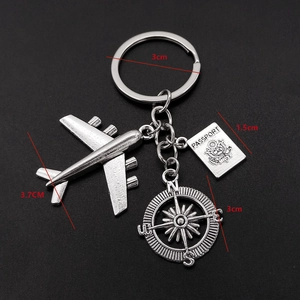 Travel keychain with airplane, compass and passport charms on black background