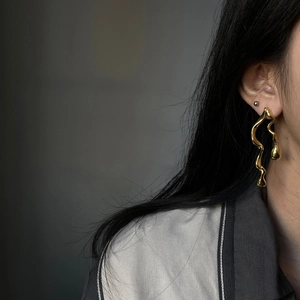 Detail shot of golden asymmetric wavy earrings with drop pendant on female model