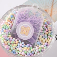 Detailed view of purple paper clips in a clear box with cartoon bear sticker in a bowl