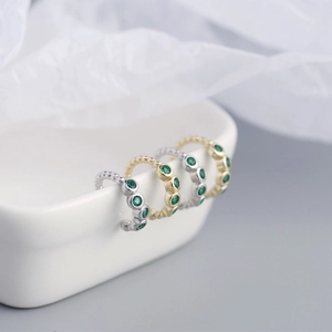 Detailed view of silver and gold cuff earrings with green gemstones on white porcelain