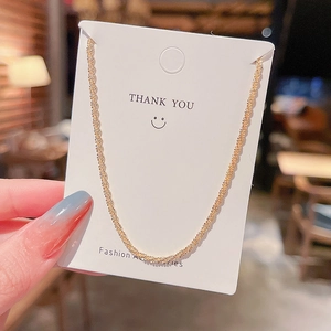 Close-up of a gold twisted rope necklace held against a Thank You card backdrop