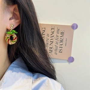 Detail of beaded Christmas wreath earrings with golden snowflake and red bow on model