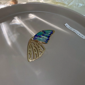 Detail of butterfly brooch featuring blue green enamel wings and gold hollow metalwork