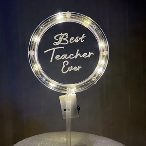 Macro shot of circular LED cake topper with warm glowing lights and Best Teacher Ever text