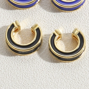 Macro view of C-shaped gold-tone ear cuffs with black and purple enamel drip finish