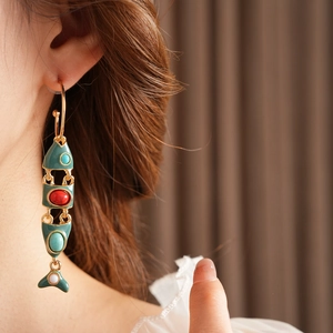 Close-up of vintage C-shaped green enamel fish earrings with colorful gems on model