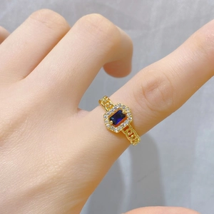 Detail eines Goldrings im Kettendesign mit rechteckigem blauen Edelstein und Diamantkranz