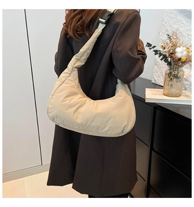Detail view of beige quilted crescent bag featuring wide shoulder strap and buckle