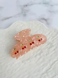 Close-up of pink marbled acetate hair claw with red and green rhinestone cherry patterns