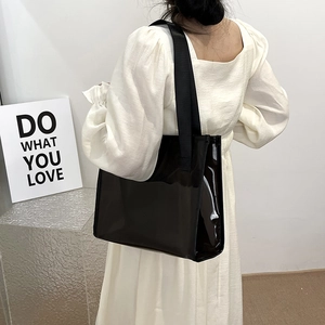 Glossy black large capacity tote bag shown on model wearing white puff sleeve dress