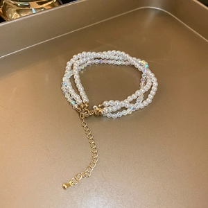 Detailed view of layered faux pearl and iridescent bead bracelet on a gold metal tray