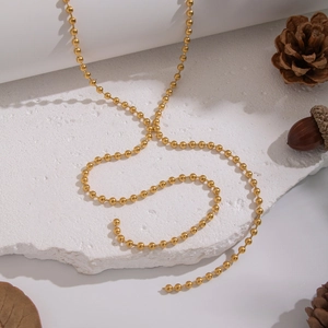 Close-up of golden beaded stainless steel necklace on white stone with pine cones