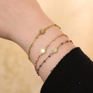 Detailed close-up of stacked gold sun charm bracelets with green, pink, and blue beads