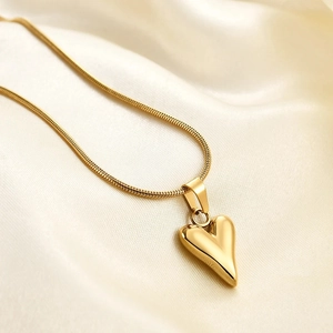 Minimalist gold heart pendant necklace on a sleek snake chain over silk background