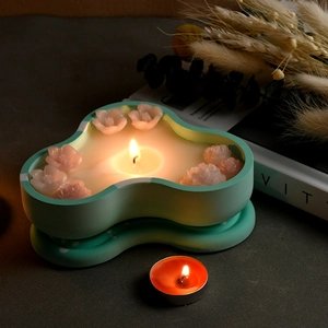 Close-up of wavy cloud-shaped mint green candle jar with pink flower wax decorations
