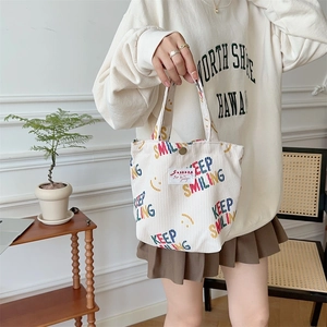 Close-up of white corduroy tote bag featuring colorful Keep Smiling prints and brand label
