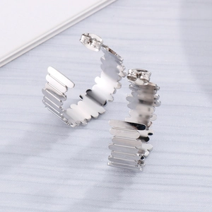 Détail de boucles d'oreilles argentées en C avec bords ondulés et une finition métallique