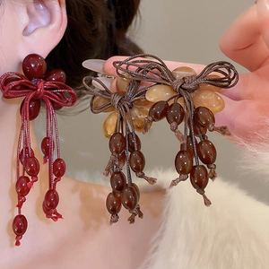 Detail of handmade woven bow earrings with wine red and amber resin tassel beads