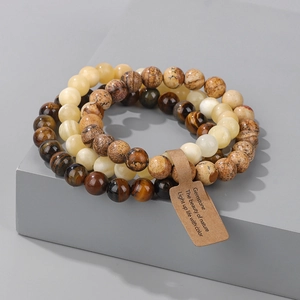 Three elastic gemstone bracelets with tiger eye and agate beads on a grey cube display