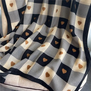 Detail of checkered scarf with brown heart patterns and black piped edges on a chair