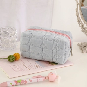 Detail of grey plush heart-quilted makeup bag with pink zipper on a desk