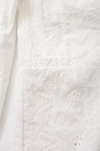 Detailed macro view of white cotton fabric with floral eyelet embroidery and hollow cutwork