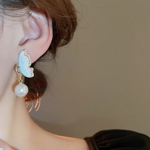 Close-up of elegant butterfly drop earrings with blue enamel and white pearl on model