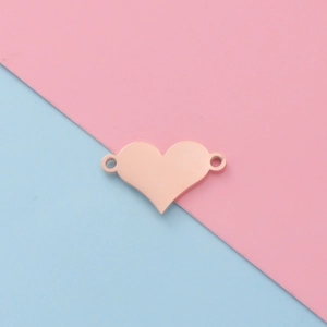 Macro view of a polished rose gold heart charm with dual holes on a pastel background