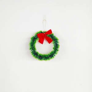 Green sequined Christmas wreath with a large red satin bow on a plain white wall