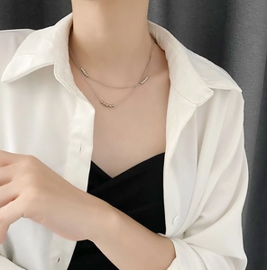 Detail of silver double-layered bead chain necklace on a neck with a white shirt